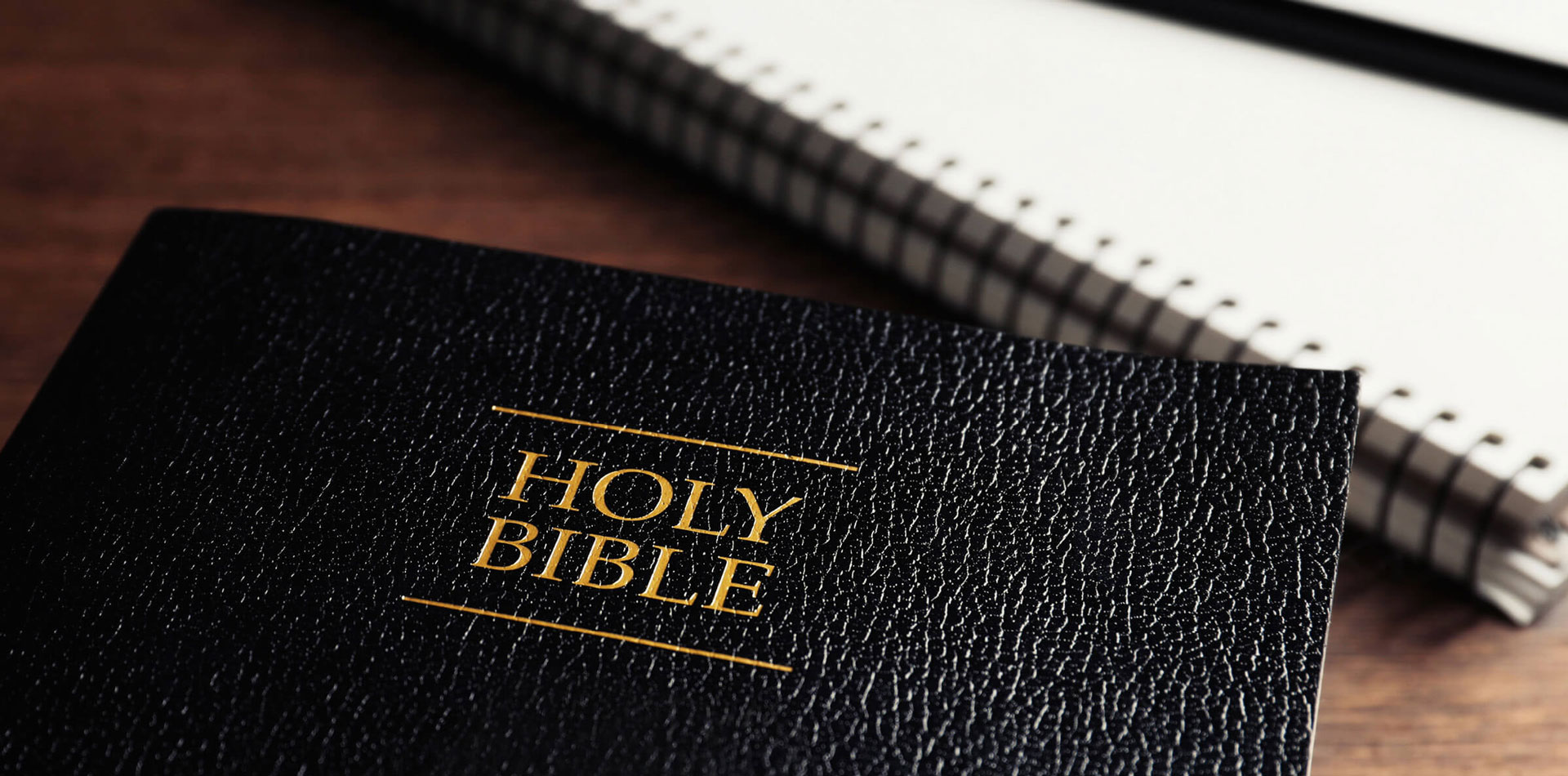 The Bible on a table next to a notebook.